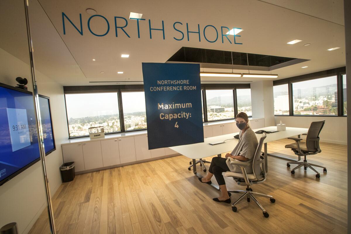 A woman sits in a conference room behind glass wall