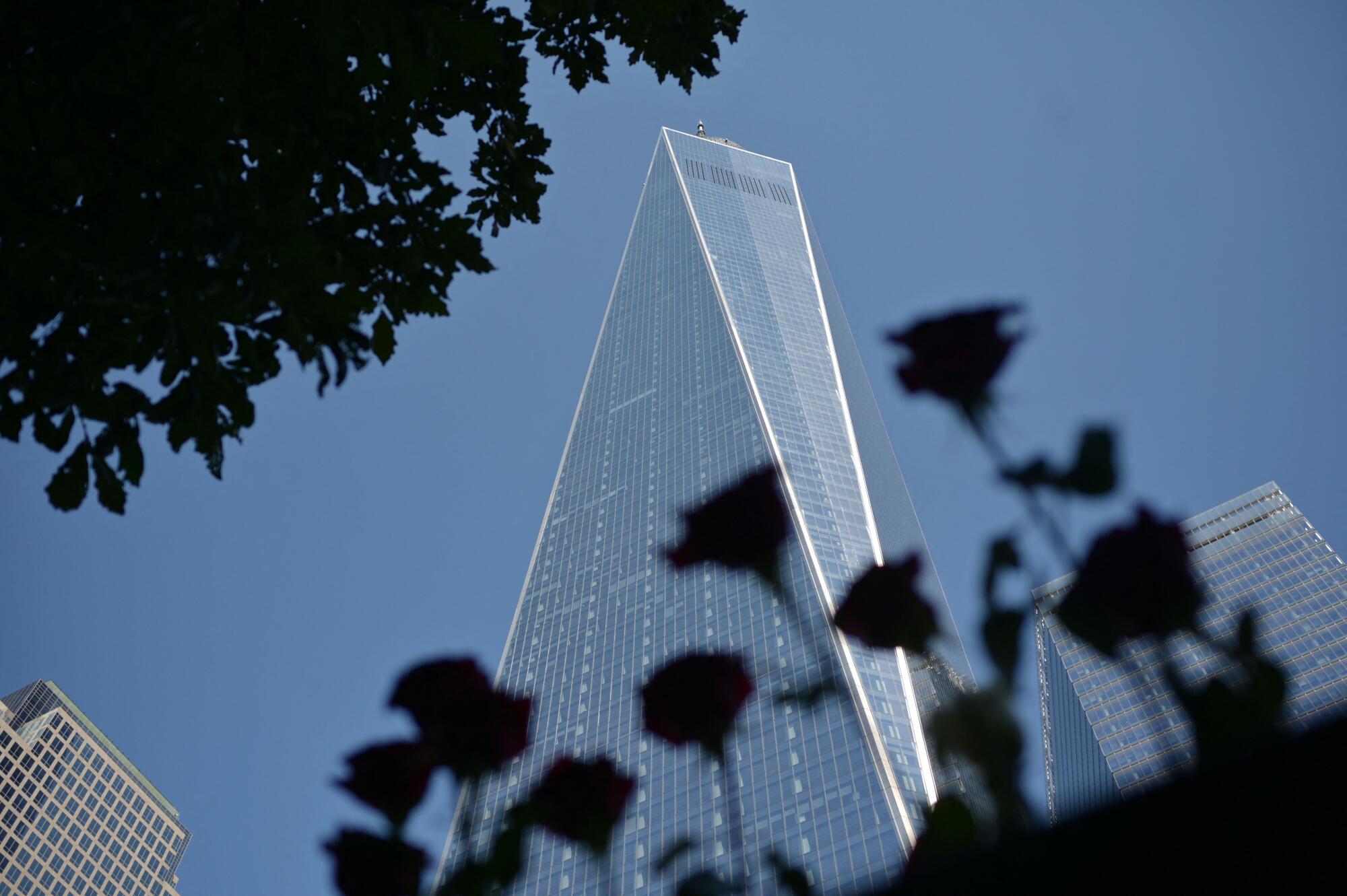 The One World Trade Center tower stands in a blue sky between other buildings.