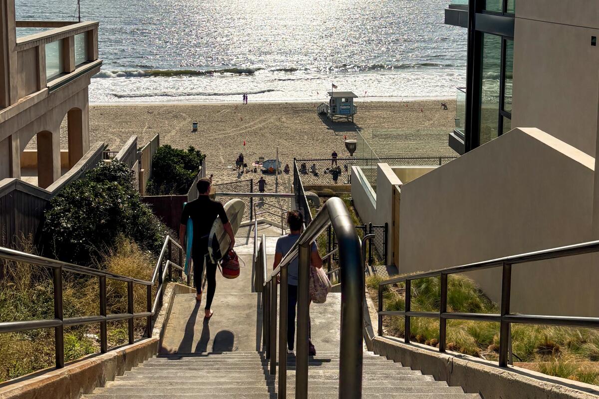A concrete staircase with a handrail in the middle, leading down to the beach and Pacific Ocean