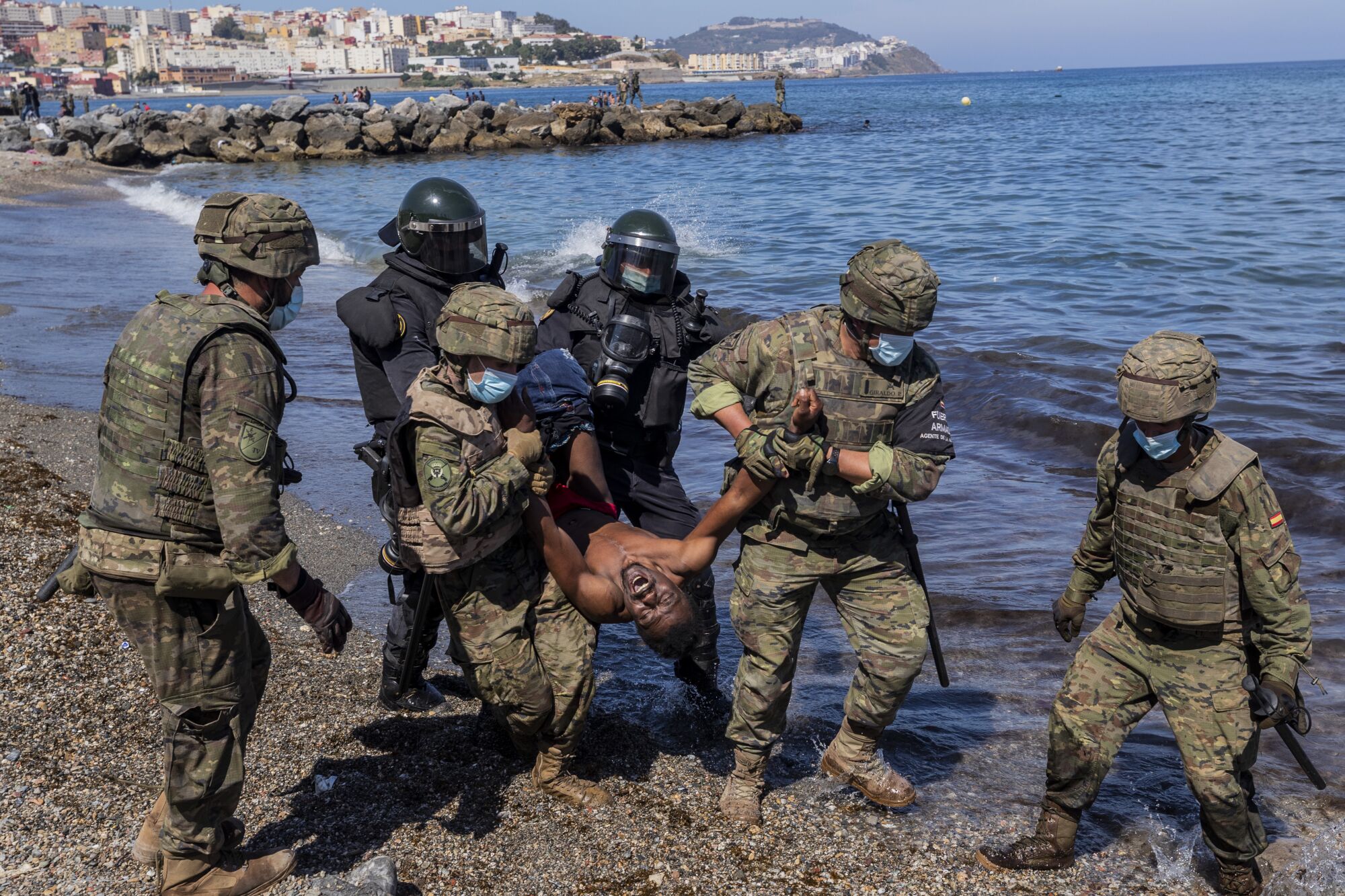 A screaming man is carried along a beach by soldiers gripping each of his limbs