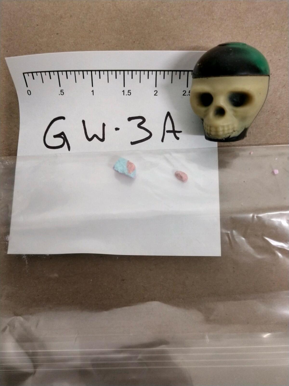 A small amount of a pink and blue substance in a plastic bag next to a silicone skull