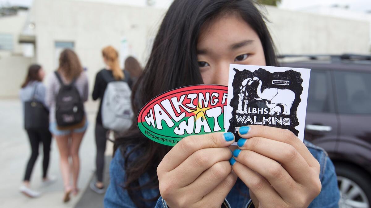Utah Urushido displays the stickers she created for the Walking for Water event Saturday at the Laguna Beach High School track.