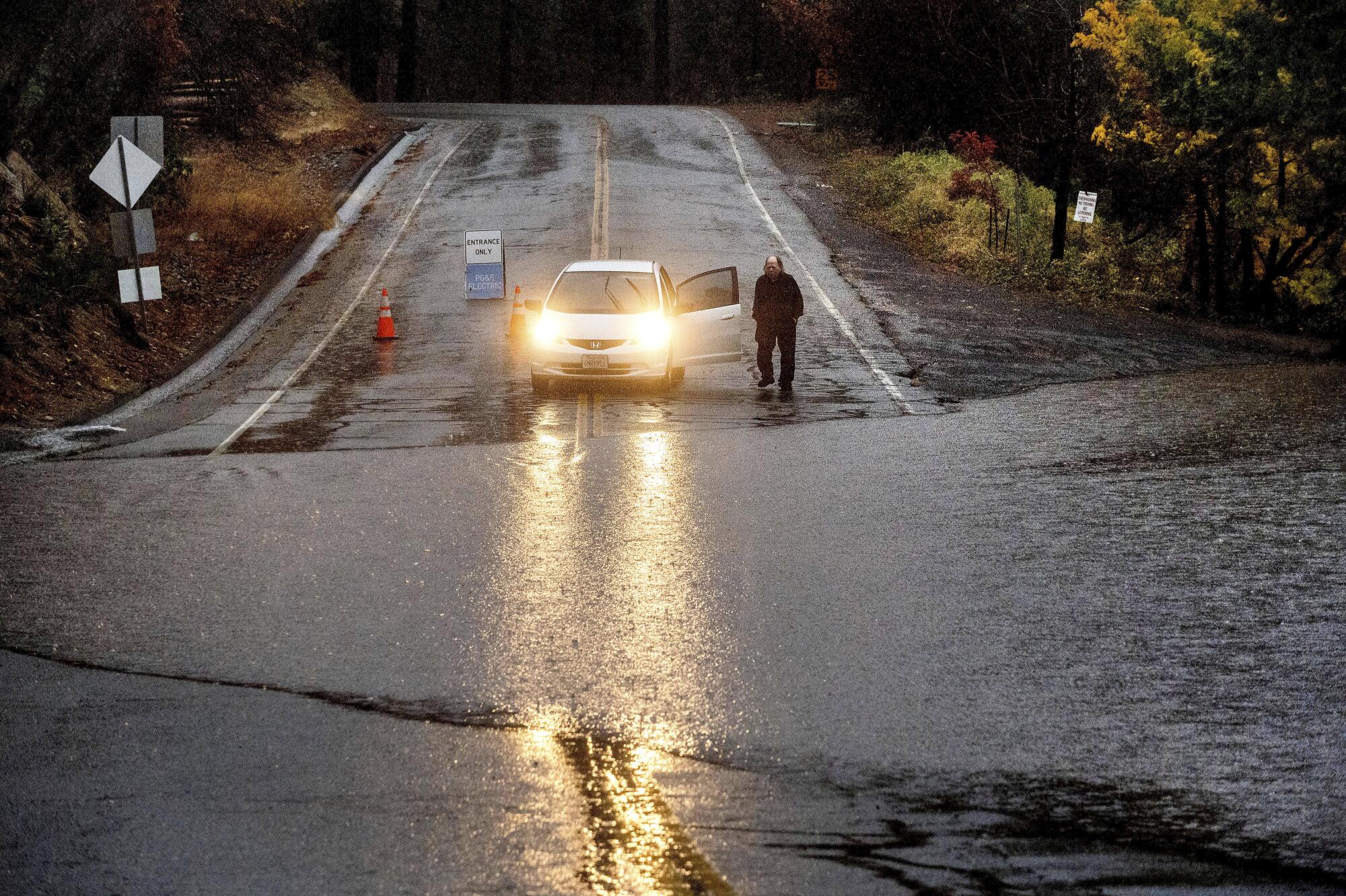 A motorist stands next to his car and surveys floodwaters crossing a street