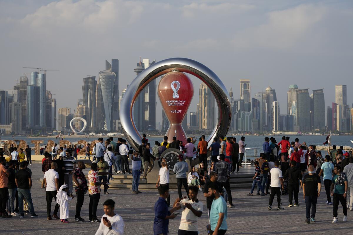 People gather around a large countdown clock beside a body of water with skyscrapers in the background