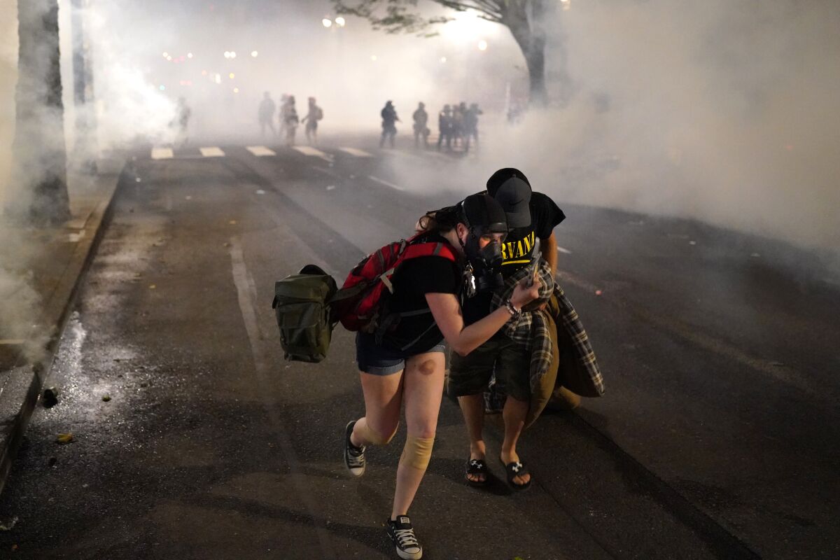 Two people protesting racial inequality in Portland, Ore., on July 21 flee after federal agents deployed tear gas.