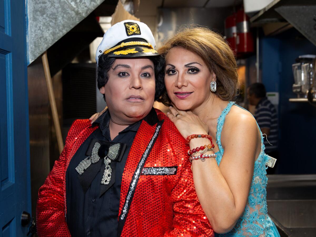 Two people in sequined outfits sit for a portrait and look straight to the camera.