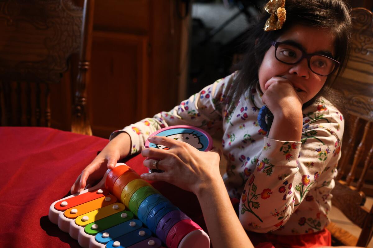 With guidance from her mother, a girl with special needs plays music on a child's xylophone at their home.