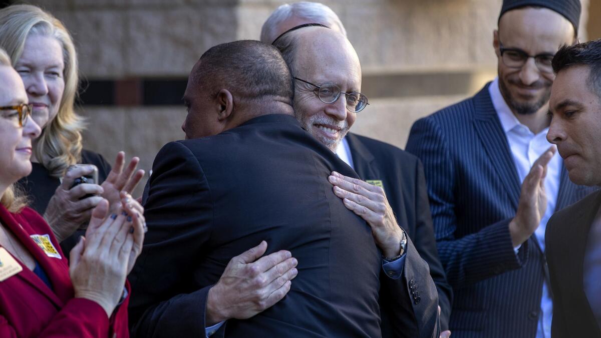 Pastor Mark Whitlock, left center, of Christ Our Redeemer AME Church, hugs Rabbi Yisroel Ciner, Beth Jacob Congregation, after they and others spoke at a news conference at the Irvine Civic Center, denouncing intolerance.