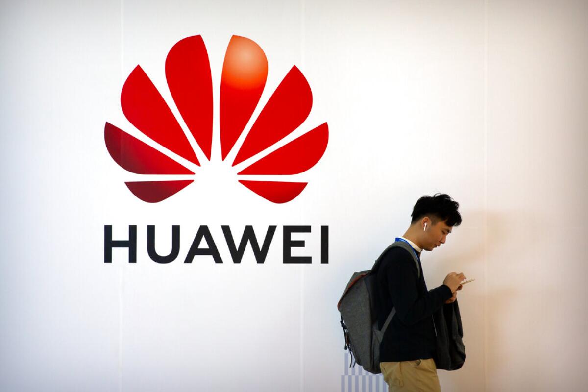 Fotografía de archivo del 31 de octubre de 2019 de un hombre usando su smartphone junto a un letrero de la firma tecnológica china Huawei en la PT Expo en Beijing. (AP Foto/Mark Schiefelbein, Archivo)
