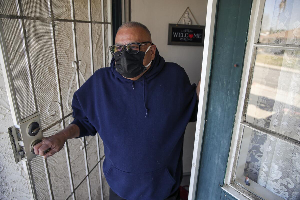 Luis Parocua opens his front door wearing a mask.