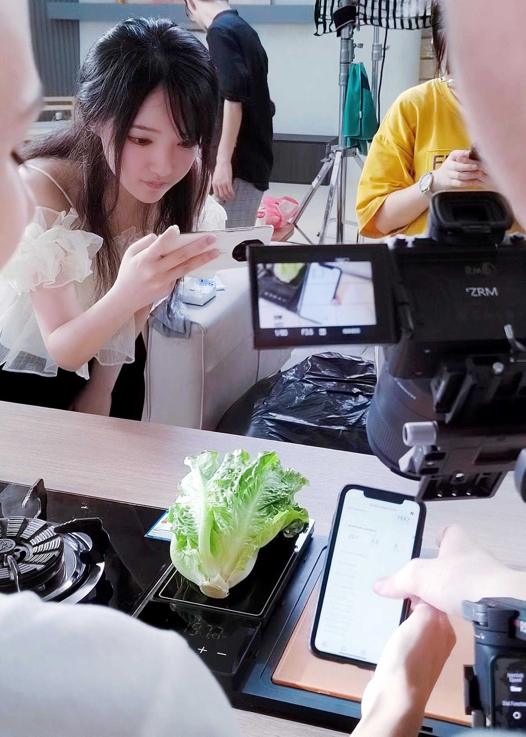 Woman taking photo of a lettuce lying on a black scale
