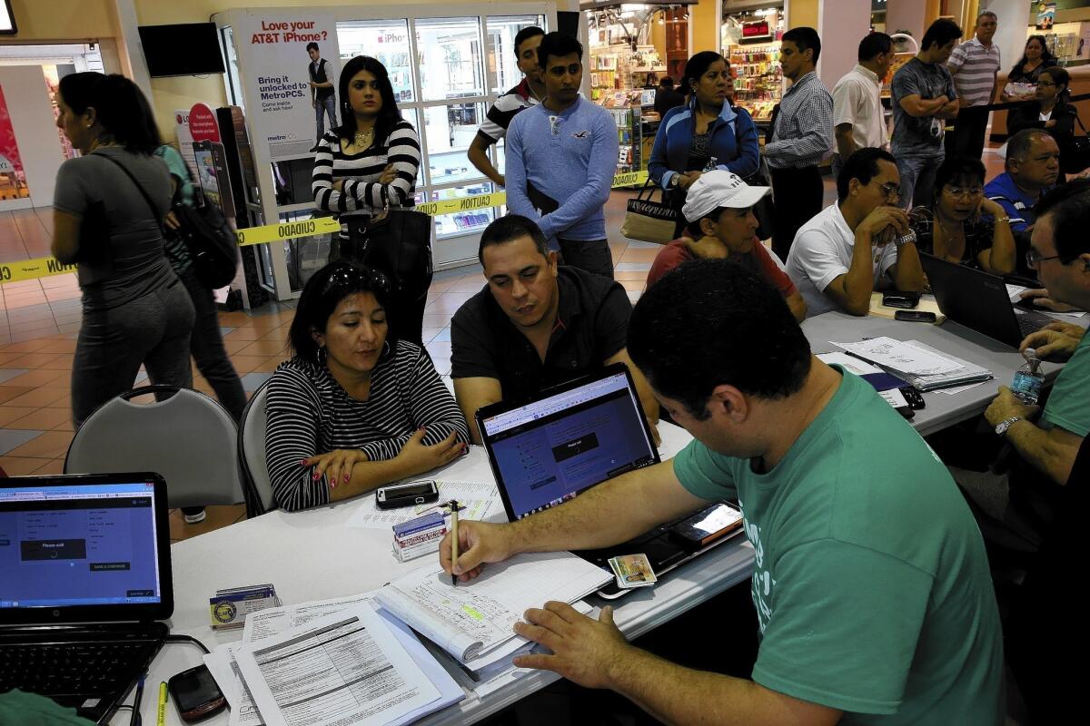 Denis Garcia of Sunshine Life and Health Advisors helps Marlene Lima-Rodriguez, left, and Javier Gonzalez buy health insurance under the Affordable Care Act, as other wait their turn, at the Mall of Americas in Miami.