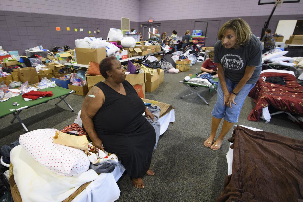 Anna Mays sits on a cot as a shelter volunteer checks on her after her home flooded recently.