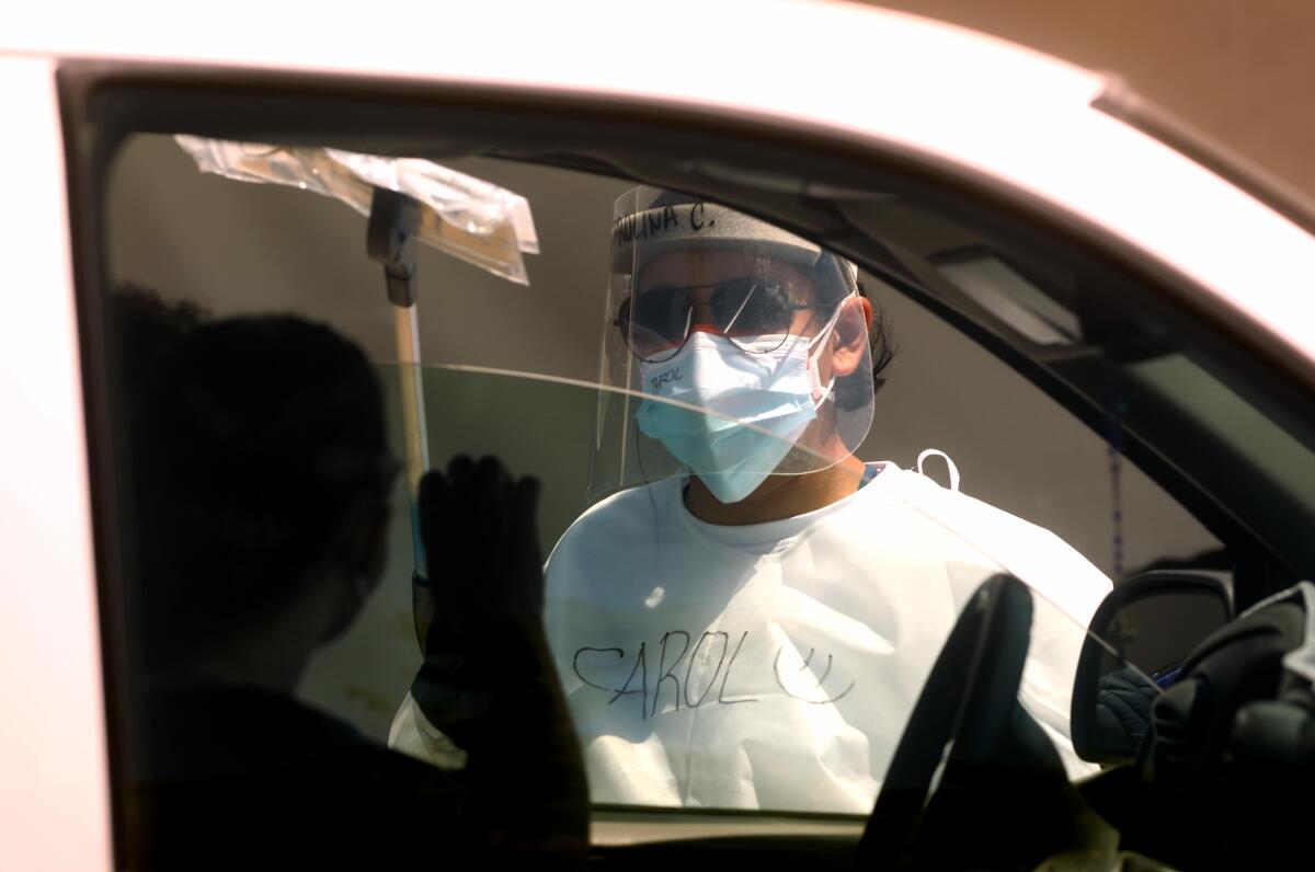 A healthcare worker passes a COVID-19 self-test kit to a participant in a car at a test site.
