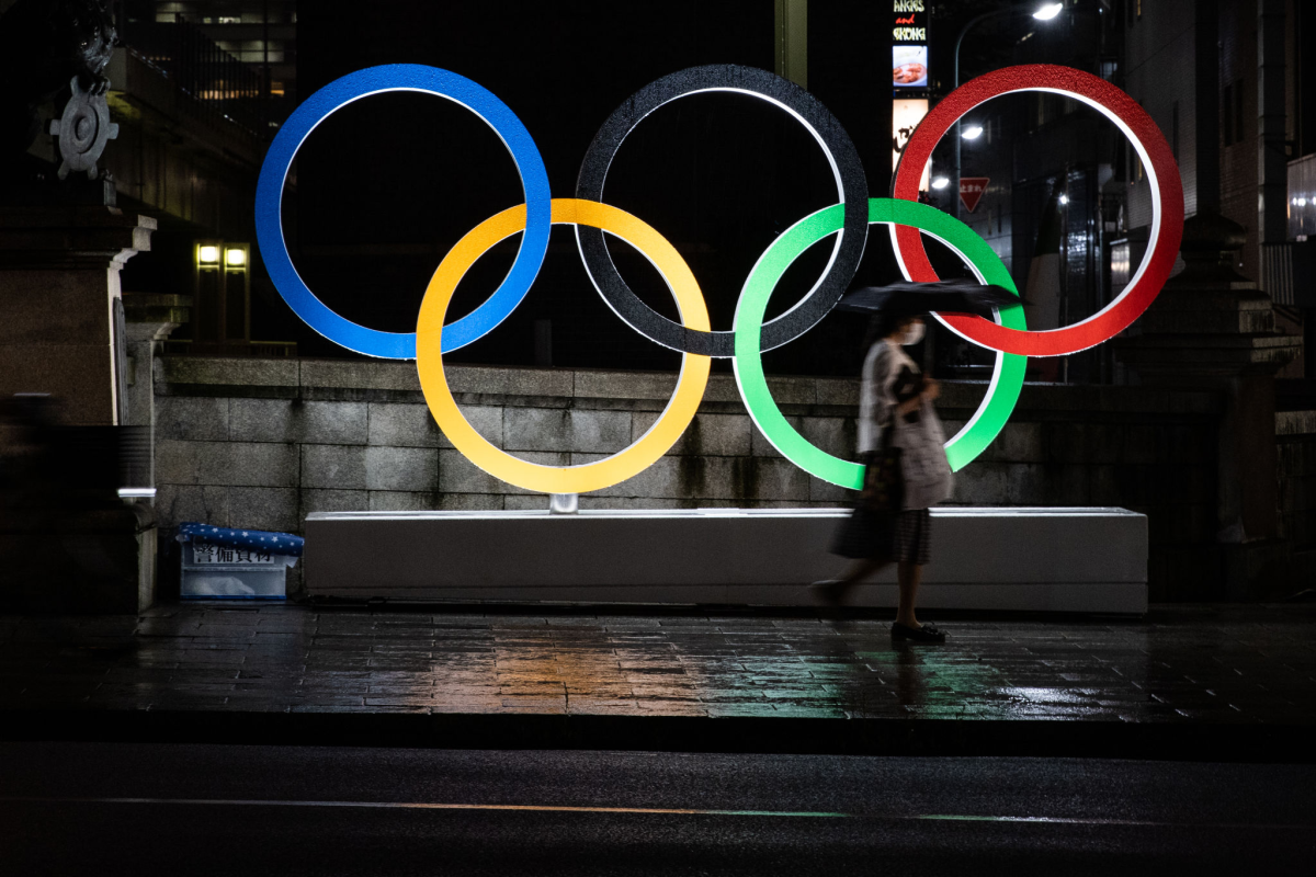 A woman wearing a face mask walks past the Olympic Rings in Tokyo, Japan.