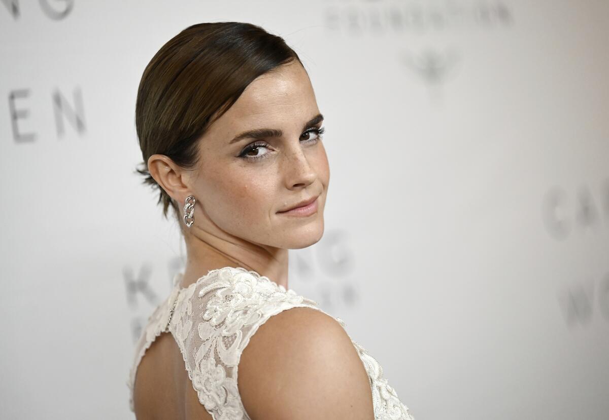 Emma Watson poses in a white lace dress while looking back over her shoulder.