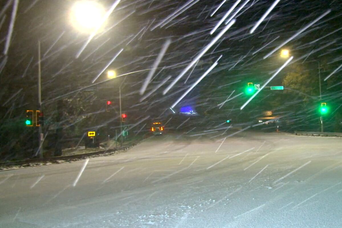 Snow falls at night over a stop-light intersection.