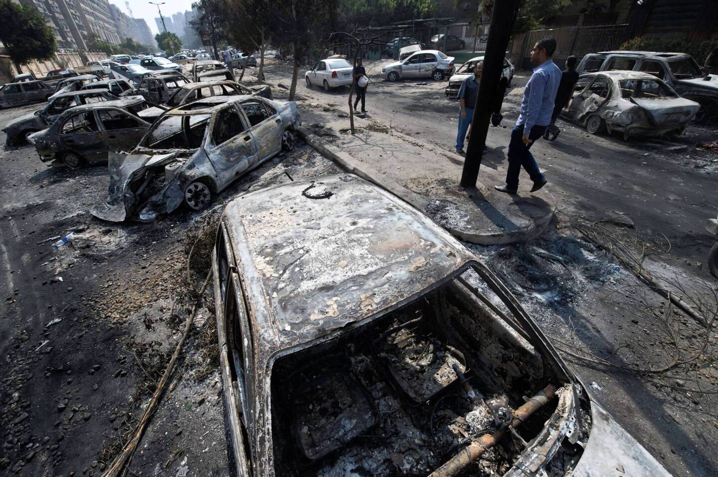Egyptians pass by burnt vehicles outside the destroyed camp of ousted Mohammed Morsi supporters outside Rabaa al-Adawiya mosque in Cairo.