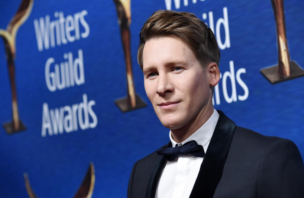 A man in a tux in front of an awards backdrop 