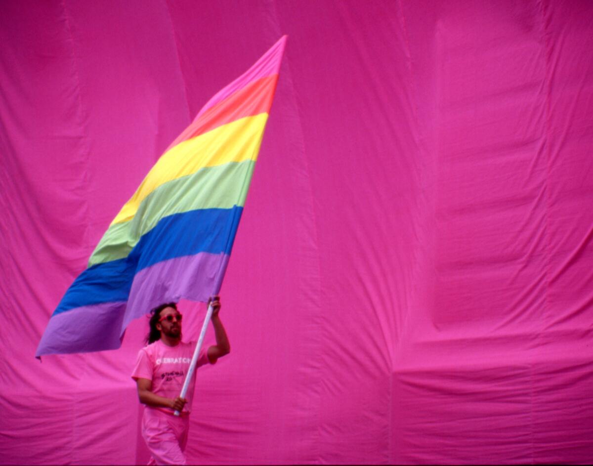 Gilbert Baker holds the rainbow flag against a pink backdrop