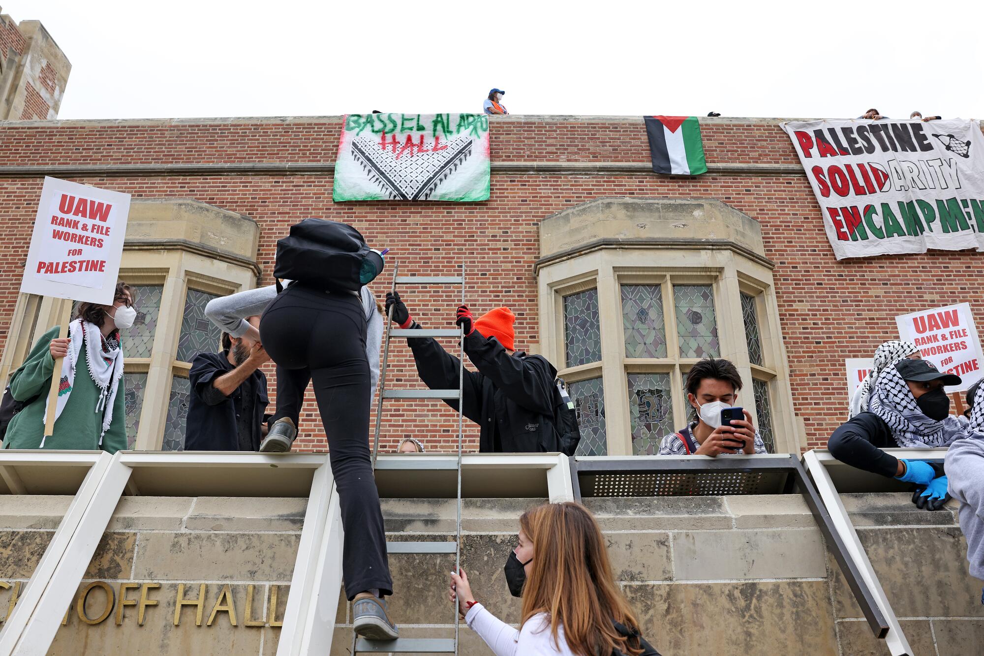 UCLA protesters climb up a ladder at Kerckhoff Hall as they try to build a new Palestinian solidarity encampment on Thursday.