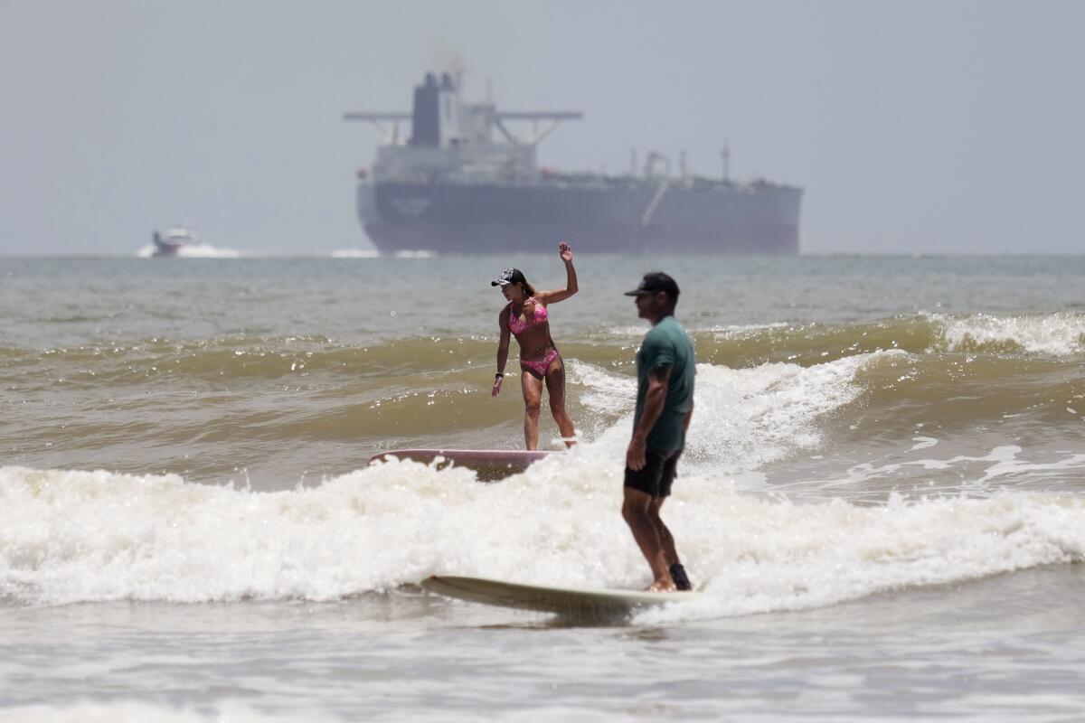 Two people surfing with an oil tanker in the distance