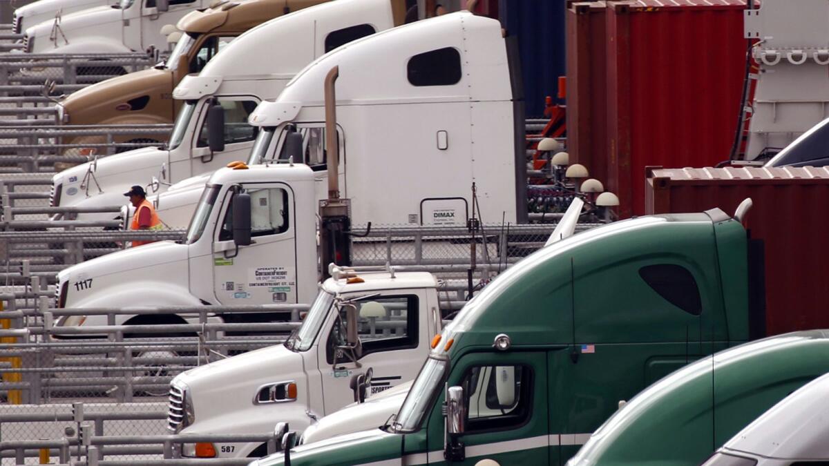 A driver walks past a row of trucks that are preparing to leave their shipping containers at the Port of Los Angeles.
