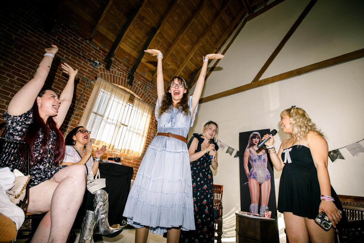 A photo of a woman posing and smiling and others cheering her on at the Taylor Swift listening party.