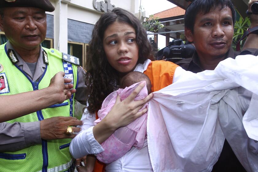 FILE - In this Tuesday, April 21, 2015 file photo, Heather Mack of Chicago, Ill., center, is escorted by police officers as he arrives in the courtroom for her sentencing hearing at a district court in Denpasar, Bali, Indonesia. Mack who was convicted of assisting her then-boyfriend in her mother's murder and stuffing the body in a suitcase on the resort island in 2014, is being released early from a 10-year sentence, a prison official confirmed Wednesday, Oct. 6, 2021. (AP Photo/Firdia Lisnawati, File)