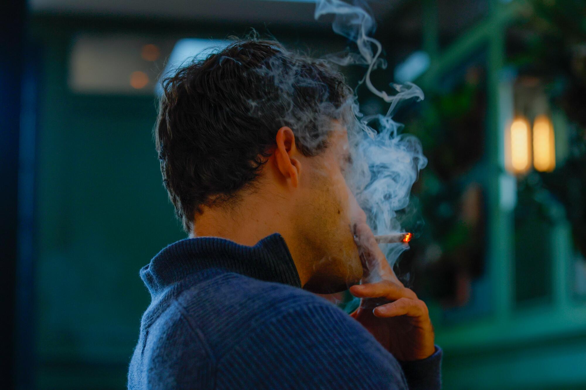 A side profile view of a man taking a drag from his joint, smoke obscuring his face.