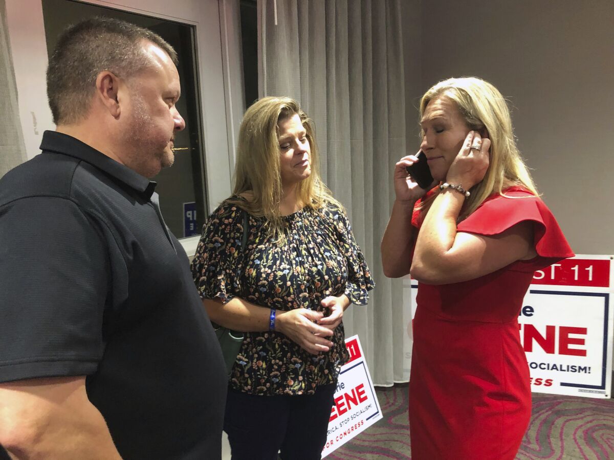 Supporters stand with construction executive Marjorie Taylor Greene, right, as she's on the phone, late Tuesday, Aug. 11, 2020, in Rome, Ga. Greene, criticized for promoting racist videos and adamantly supporting the far-right QAnon conspiracy theory, won the GOP nomination for northwest Georgia's 14th Congressional District. (AP Photo/Mike Stewart)