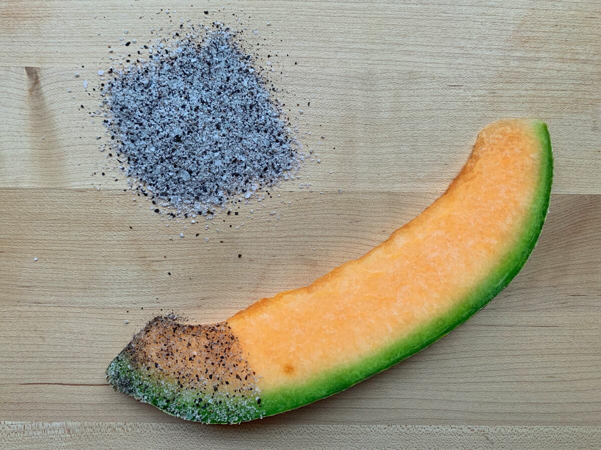 A slice of orange melon, one end dipped in a gray spice blend