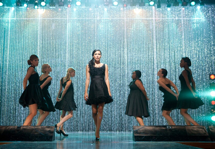 Naya Rivera performs in a short black dress surrounded by "Glee" cast