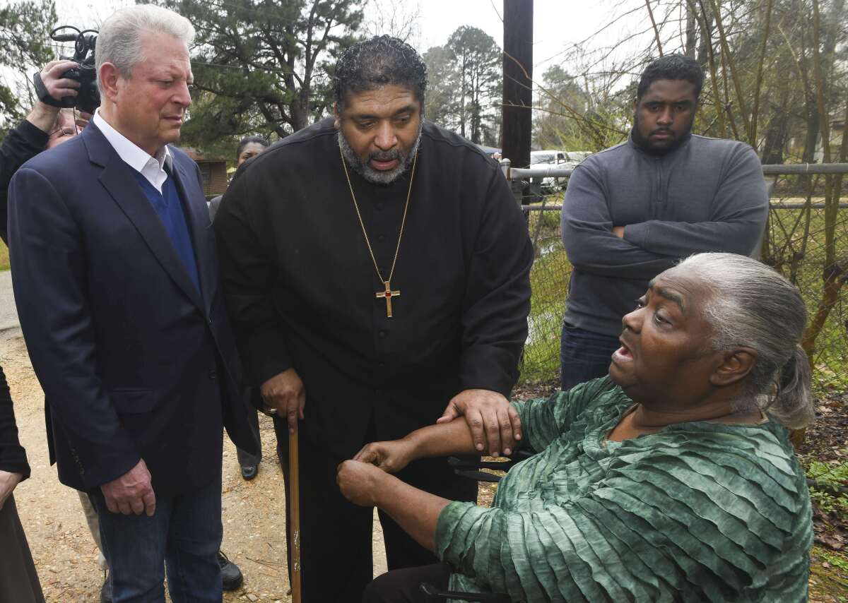 FILE - In this Feb. 21, 2019, file photo, former Vice President Al Gore, left, founder of the Climate Reality Project, and the Rev. William Barber II, president of the Repairers of the Breach, visit Lowndes County resident Charlie Mae Holcombe to talk about the failing wastewater sanitation system at her home in Hayneville, Ala. An anti-poverty coalition led by Barber is scheduled to hold a virtual march Saturday. The Mass Poor People’s Assembly & Moral March on Washington aims to build upon the nation’s principles to pursue solutions to poverty — something advocates say is getting especially severe in rural areas. (AP Photo/Julie Bennett, File)