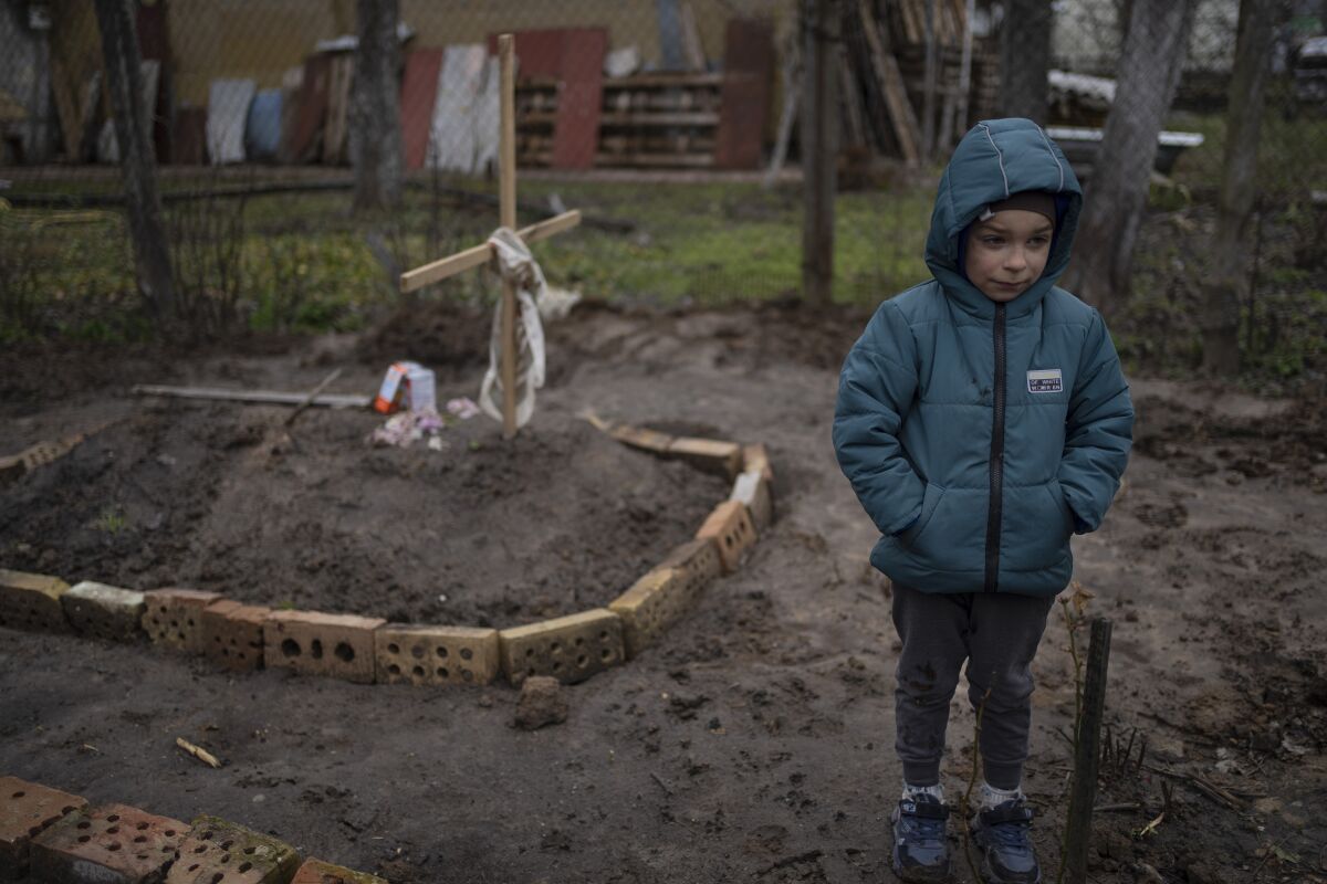 FILE - In the courtyard of their house, Vlad, 6, stands near the grave of his mother, who died, on the outskirts of Kyiv, Ukraine, Monday, April 4, 2022. Vlad's mother died last month when the family was forced to shelter in a basement during the occupation by the Russian army. The family still doesn't know what illness caused her death. (AP Photo/Rodrigo Abd)