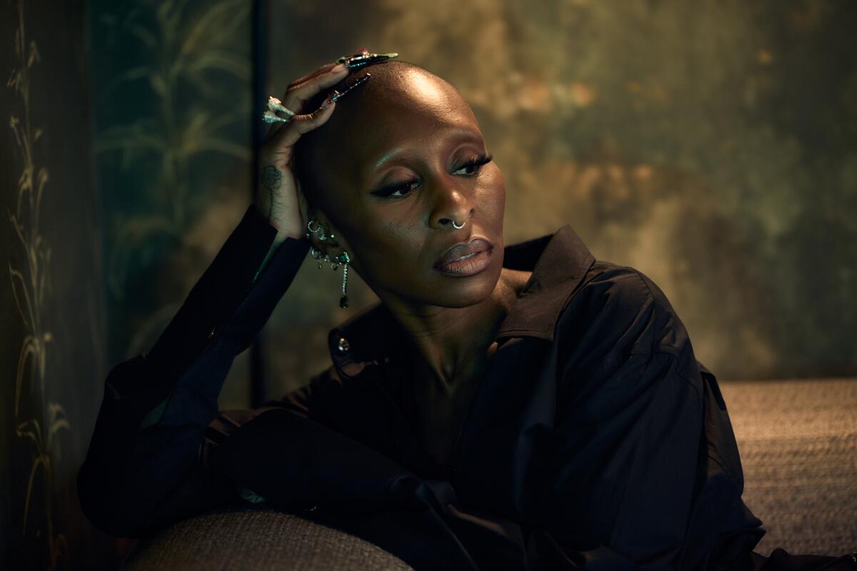 Cynthia Erivo sits looking pensively to one side, her hand resting on top of her head