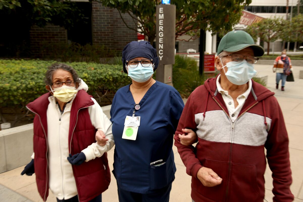 A woman in scrubs walking with her elderly parents.
