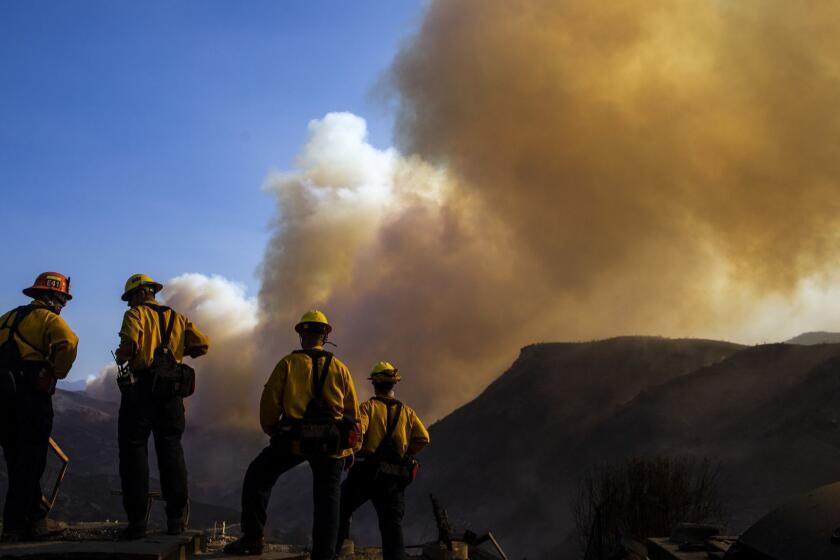 LOS ANGELES, CALIF. - NOVEMBER 11: Fire Fighters working to put out hotspots in and around structures destroyed by the Woolsey Firewatch as a plume of smoke rises from near the Chatsworth reservoir, in West Hills, on Sunday, Nov. 11, 2018 in Los Angeles, Calif. (Kent Nishimura / Los Angeles Times)