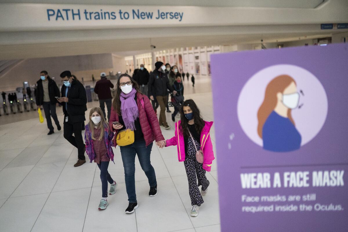 Masked people walking indoors near an overhead sign that reads, PATH trains to New Jersey 