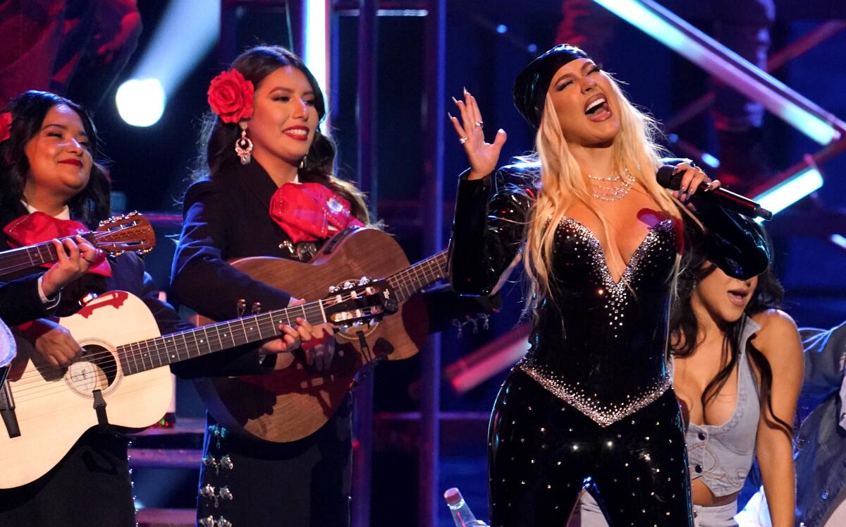 A female singer performs onstage with mariachi guitarists