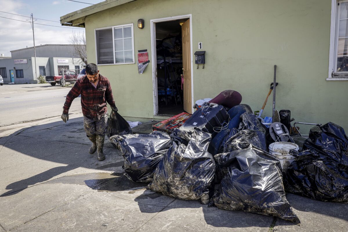 Jose Mendoza throws away destroyed belongings from his flooded home where he lives with his wife and two children in Pajaro, Calif., Thursday, March 23, 2023. Evacuation orders for Pajaro residents have been lifted since a levee breach flooded the area nearly two weeks ago. Residents are allowed to return to their homes and business to clean and gather belongings, but are advised not to stay as living conditions in some areas remain hazardous and water unsafe to drink. (Brontë Wittpenn/San Francisco Chronicle via AP)