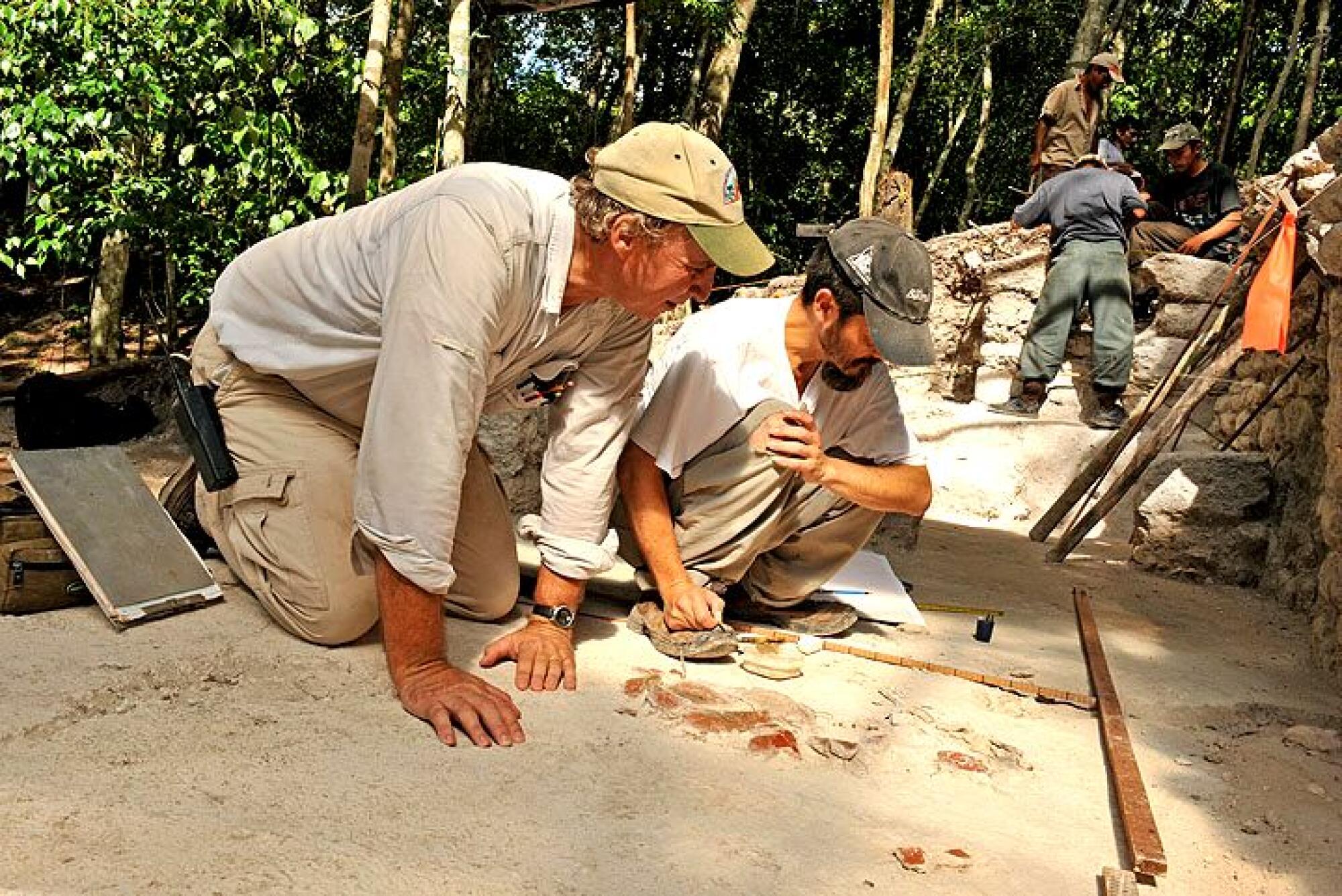 Two men look at objects on the ground 