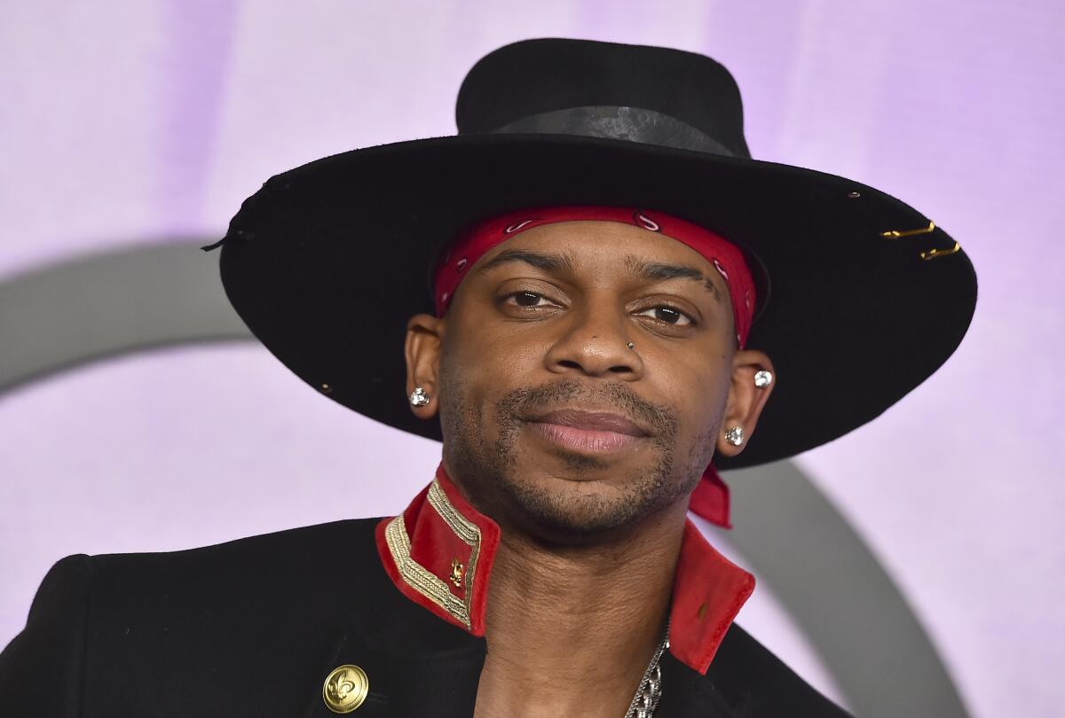 Jimmie Allen wearing a wide-brimmed black hat  and a black coat with a red collar