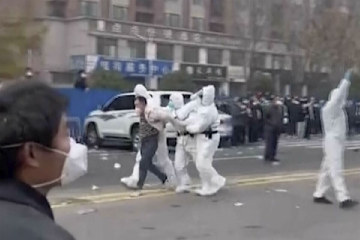 In this photo provided Nov 23, 2022, security personnel in protective clothing were seen taking away a person during protest at the factory compound operated by Foxconn Technology Group who runs the world's biggest Apple iPhone factory in Zhengzhou in central China's Henan province. Employees at the world's biggest Apple iPhone factory were beaten and detained in protests over pay amid anti-virus controls, according to witnesses and videos on social media Wednesday, as tensions mount over Chinese efforts to combat a renewed rise in infections. (AP)