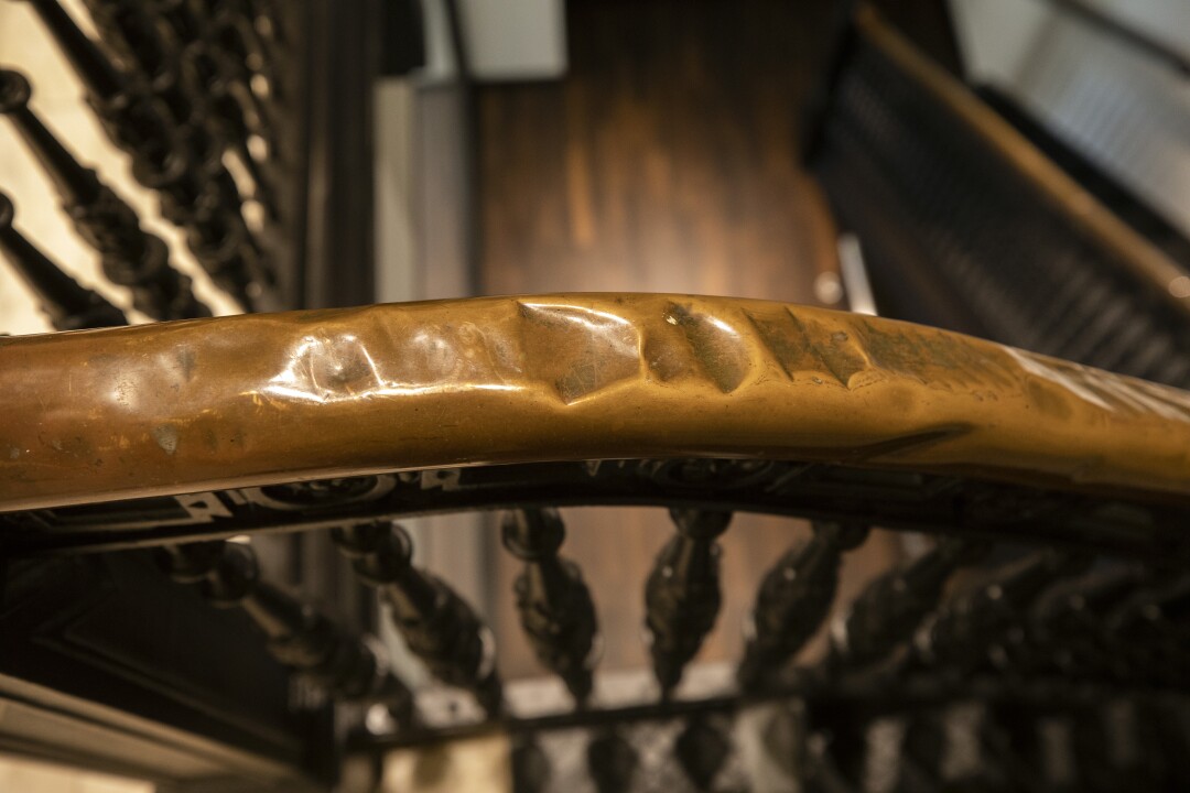 A bumpy brass banister is seen topping the balustrades of a wooden staircase