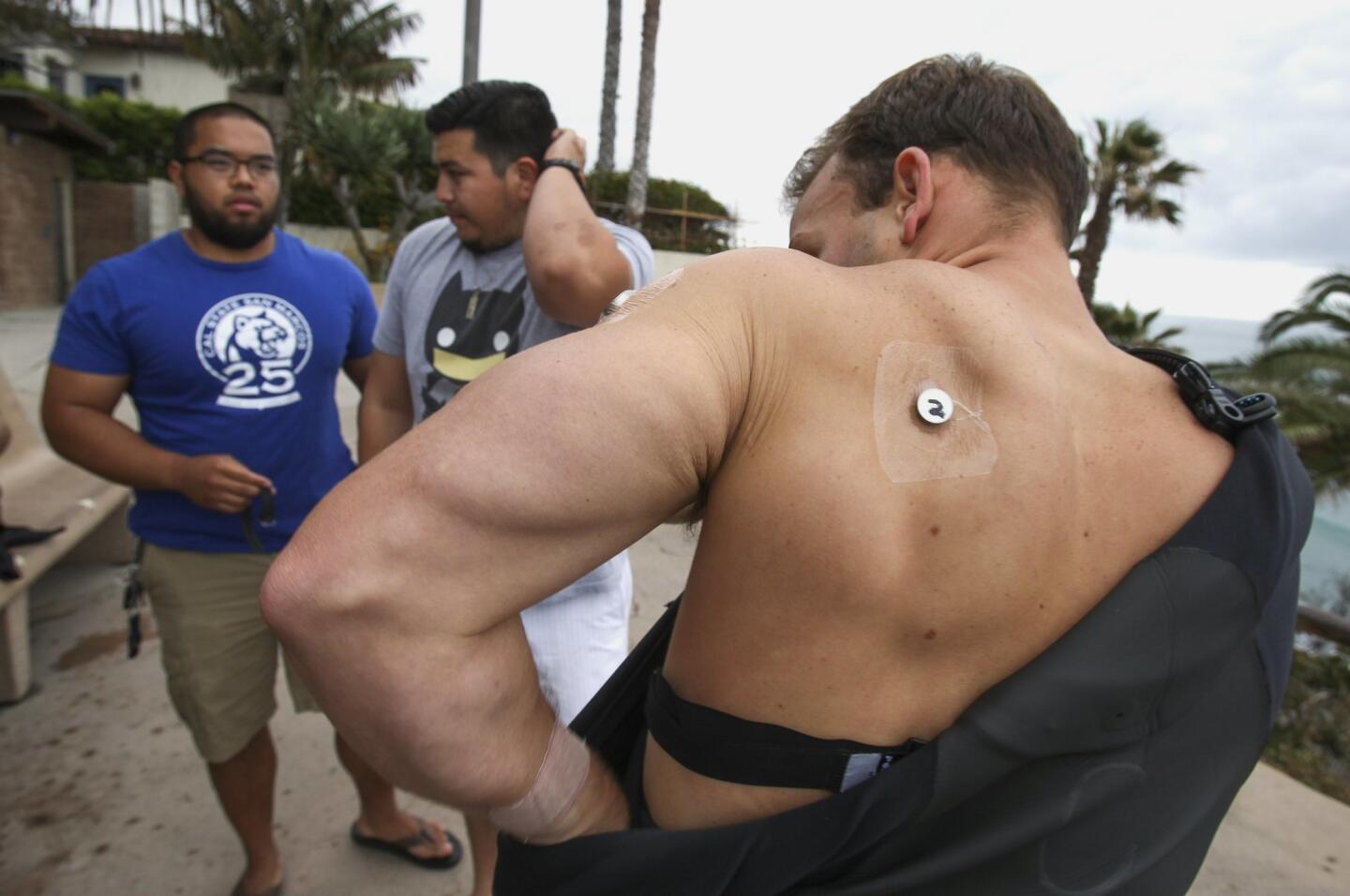 After CSUSM kinesiology students, including Alvin Padilla, 24, left, and Chris Zepeda, 24, center, placed eight skin sensors on him, surfer James Petracca, 27, puts on a Hurley wetsuit provided by the students.