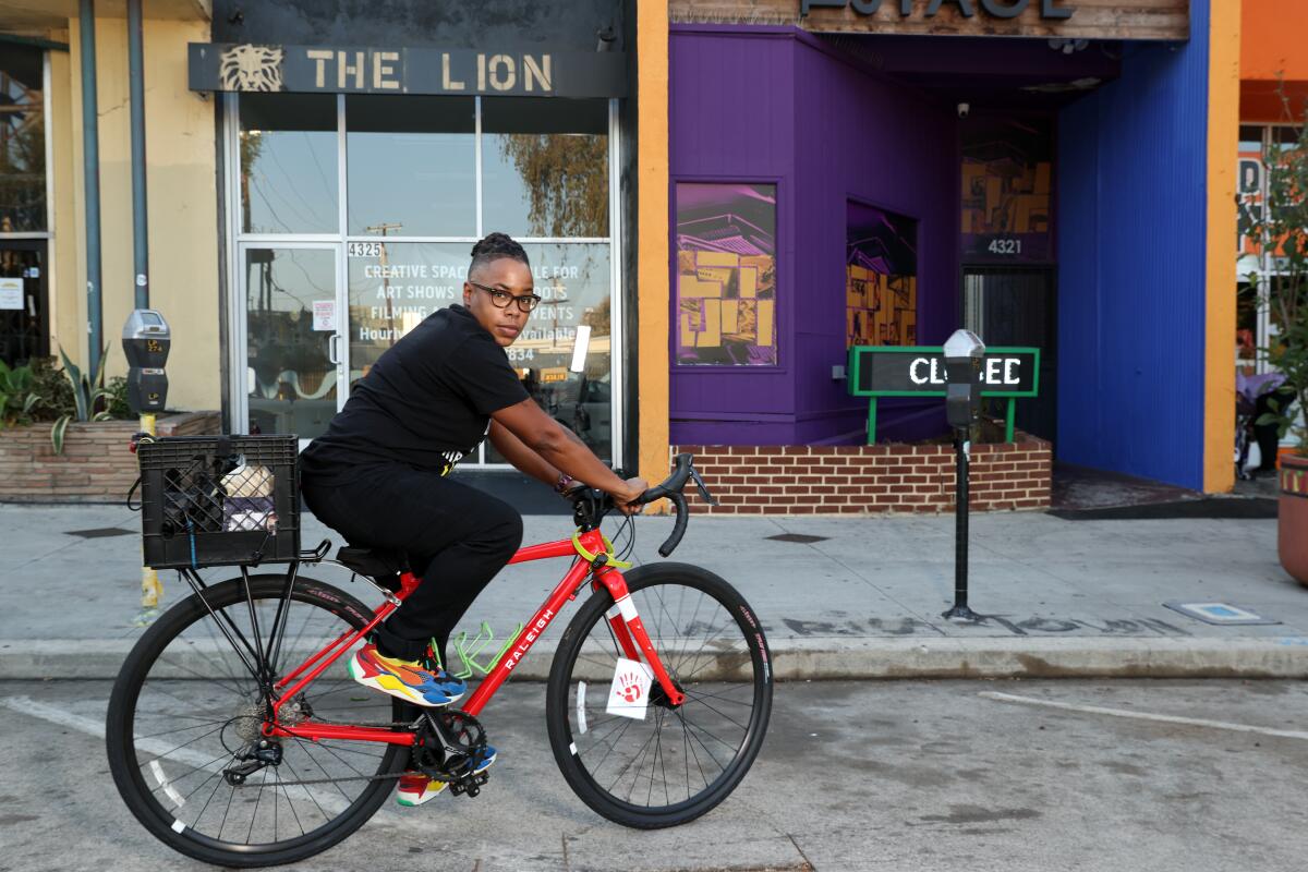 Lena Williams rides their bike past a storefront in Leimert Park in September 2020