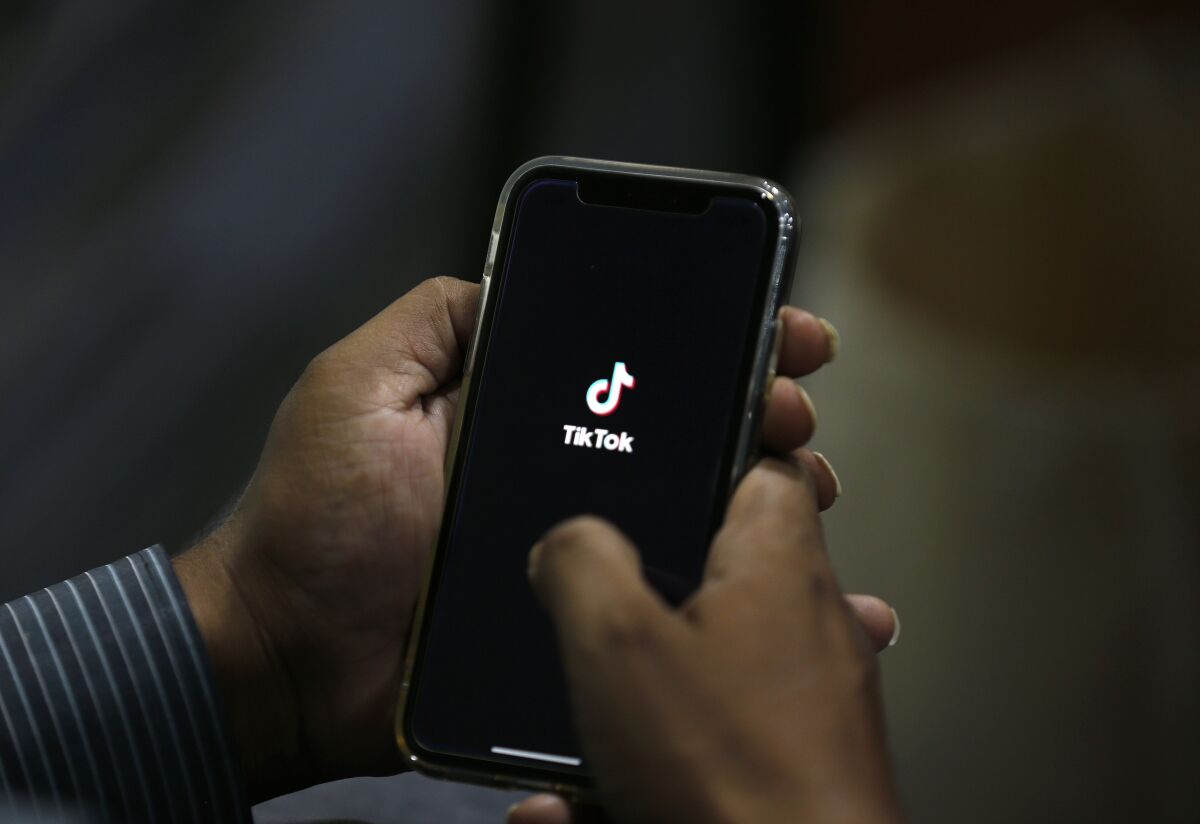 A person hold a cell phone with the TikTok icon showing on the screen. 