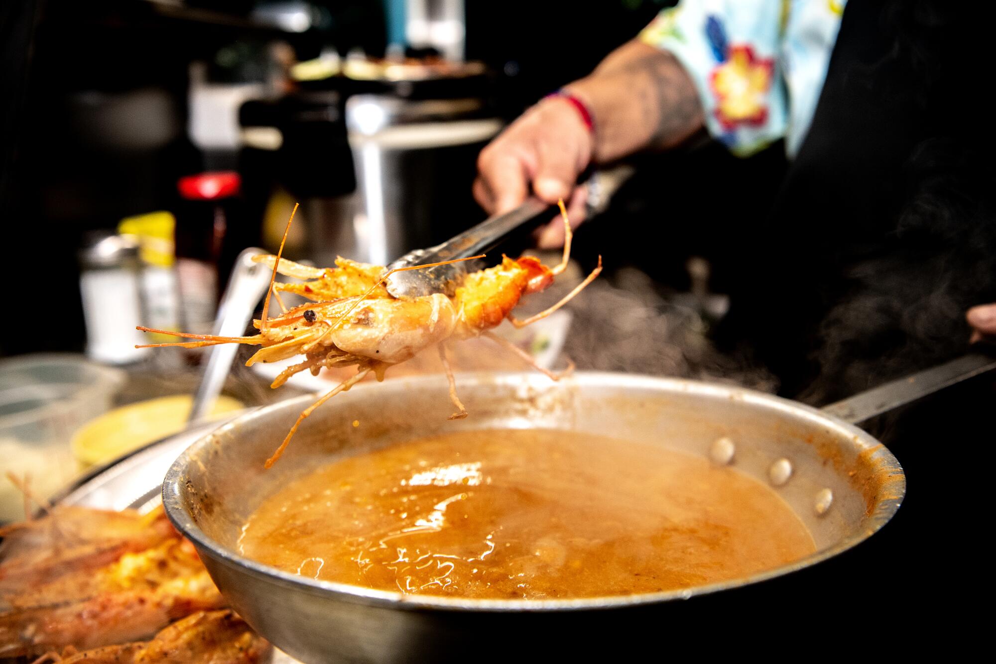 A hand uses tongs to hold a crustacean over a pot of hot liquid