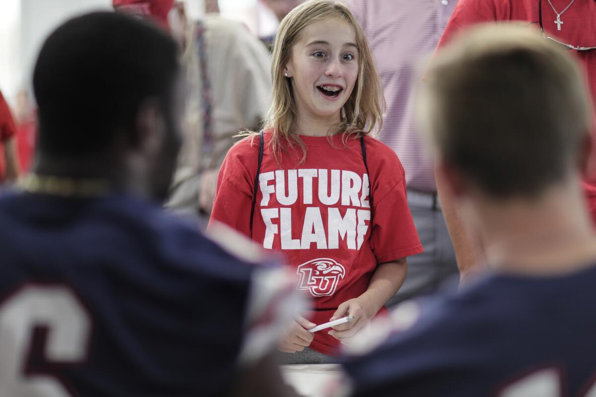 Liberty University football fan Avery Stengel, 13, excitedly asks for autographs from the quarterback group at a fan appreciation event.